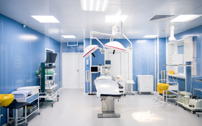 Interior of surgery room in modern clinics with all necessary equipment along walls and surgical table in center with lamps above